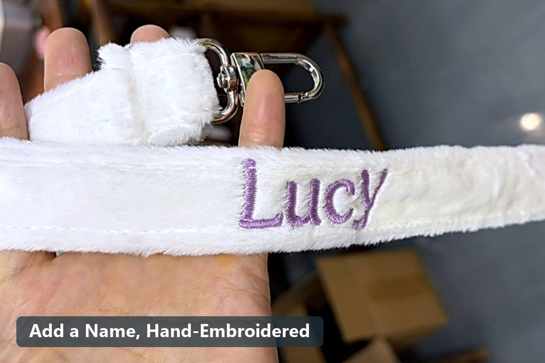 White plush backpack strap with a hand-embroidered name in purple thread - Chobyner workshop